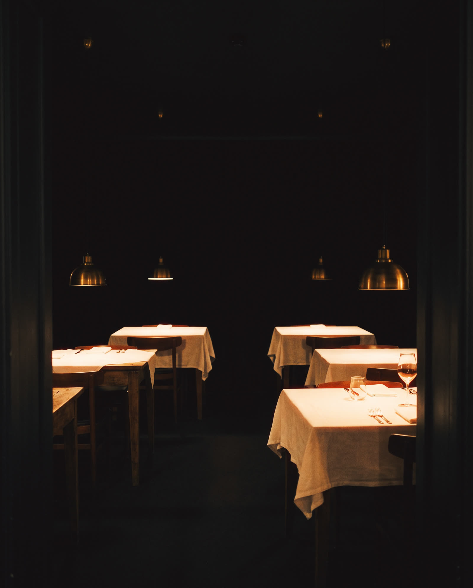 An empty dining room at night, four tables each under its own lamp