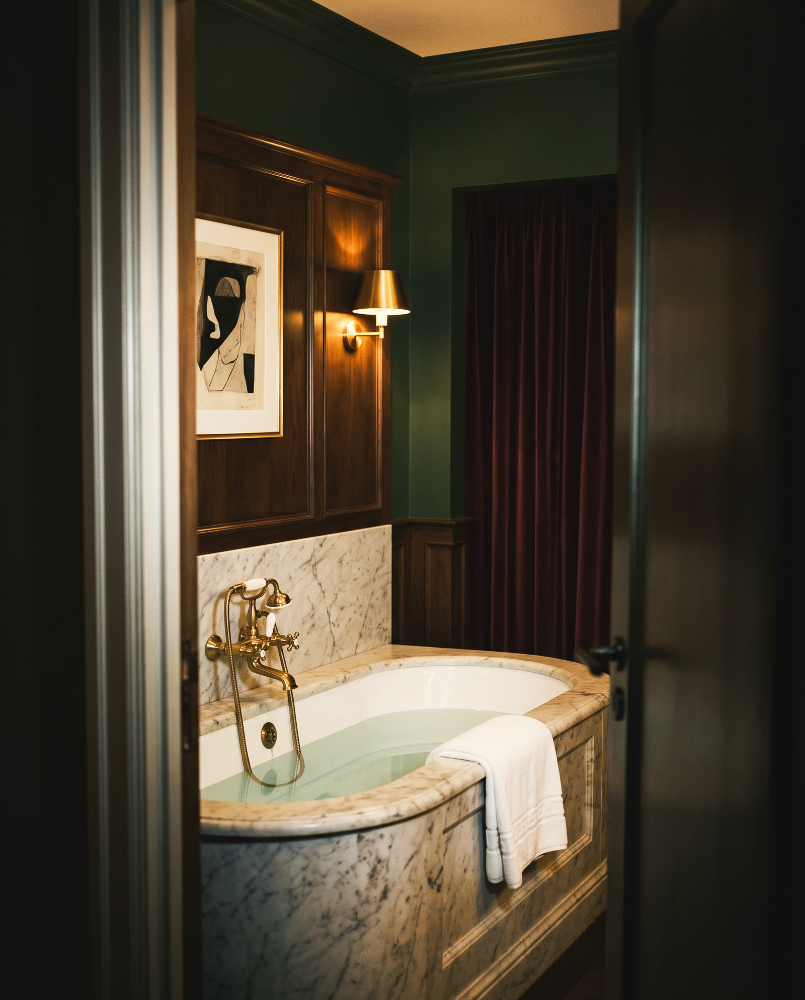 A marble bathtub with brass taps and a folded towel, seen through the door