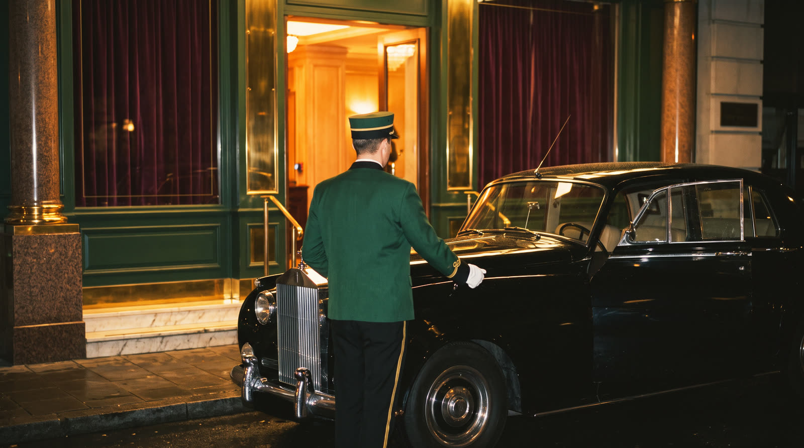A vintage car at the hotel entrance at night, the doorman opening the door