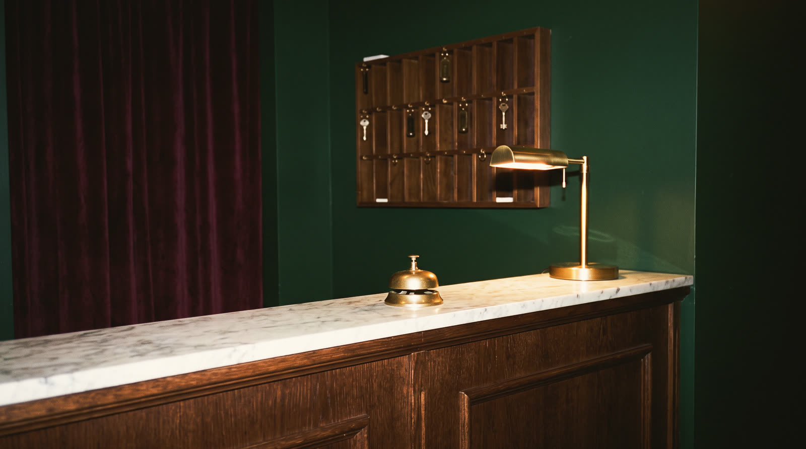 A marble reception desk with a brass bell, a lamp and a key rack behind