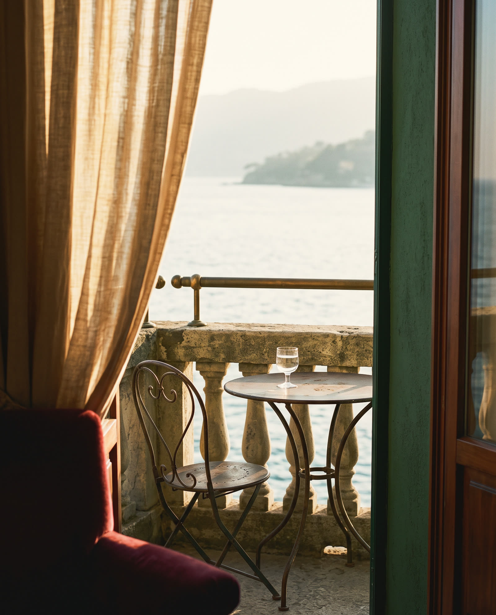 A bistro table and chair on a stone terrace above the sea, seen through a linen curtain