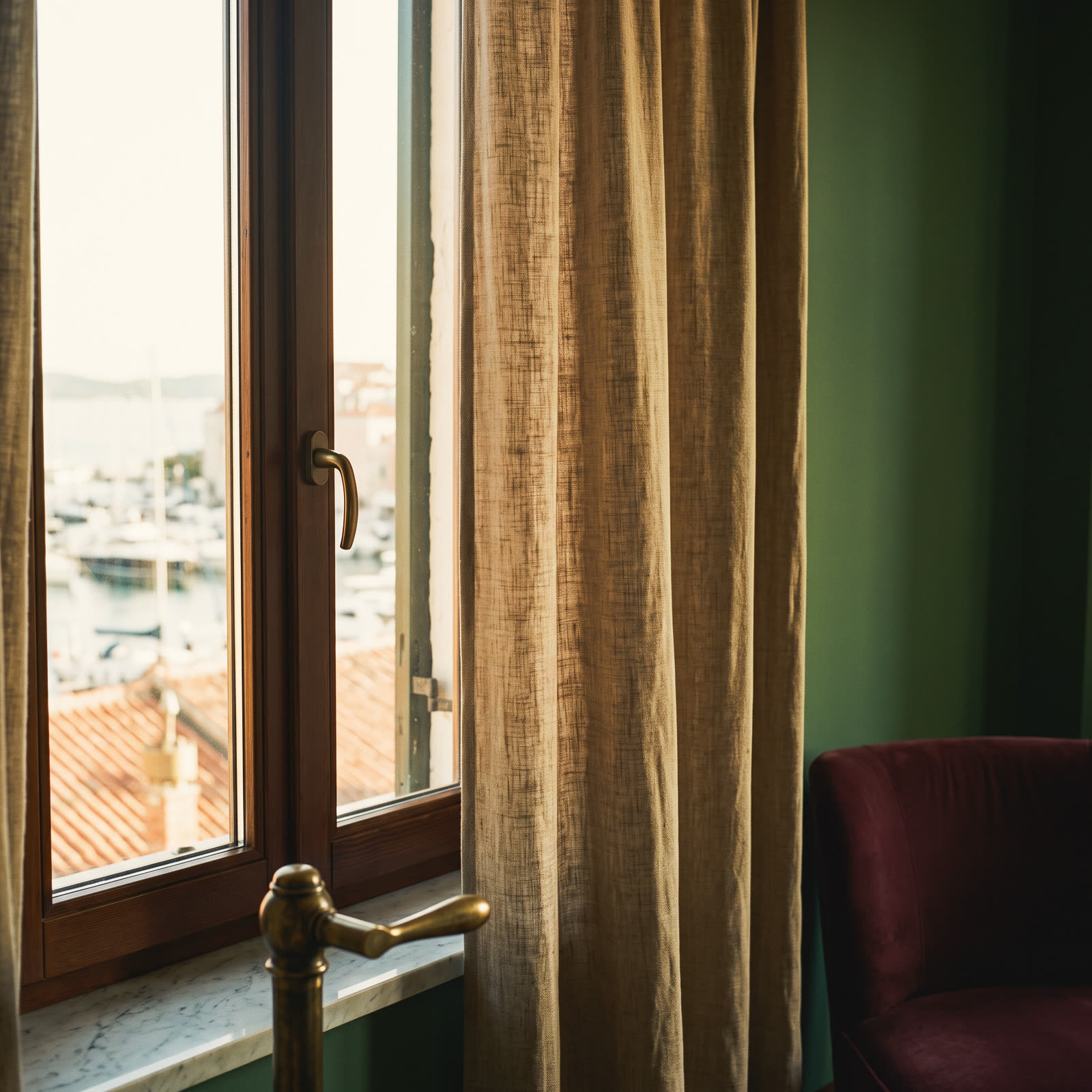 A tall window with a linen curtain, the harbour and roofs outside at dawn